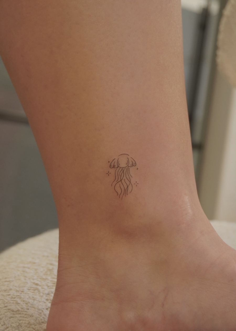 Fine line tattoo of a minimalist jellyfish with sparkles, ankle