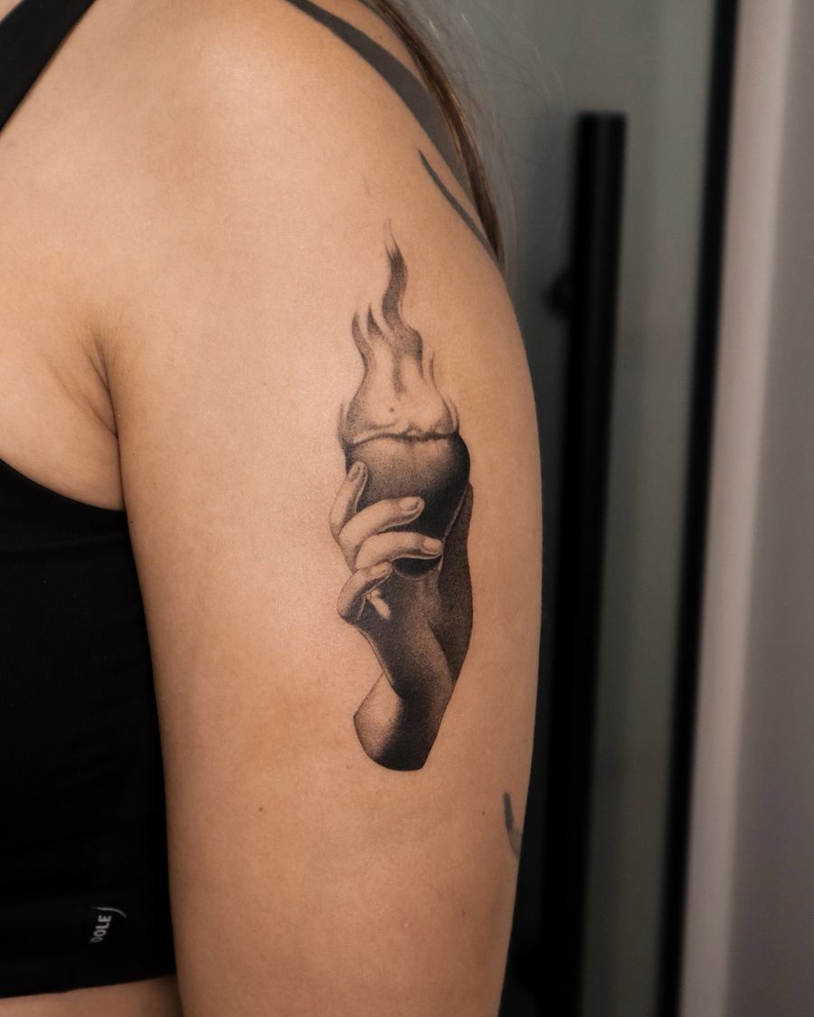 Black and grey tattoo of a hand holding a lit candle, arm